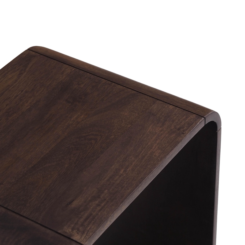 Op de afbeelding: Een donkerbruine houten bijzettafel met een gebogen ontwerp. De tafel heeft een glad, gepolijst oppervlak en een moderne uitstraling. De houtnerf is zichtbaar en voegt textuur toe aan het stuk.