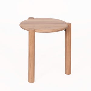 May include: A light brown wooden side table featuring a circular top surface supported by three cylindrical legs. The legs are attached to the outer edge of the round tabletop, creating a simple structure with a smooth, natural wood grain finish.