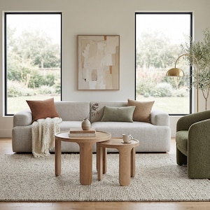 May include: A contemporary living room featuring a light grey sofa, two wooden side tables, and a textured rug. The sofa is decorated with brown and green cushions. A gold floor lamp and a green armchair complete the neutral-toned space.
