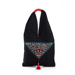 May include: Black tote bag with a red handle and a colorful embroidered triangle design. The embroidery features floral and geometric patterns in shades of blue, green, pink, and red. A red tassel hangs from the bottom.