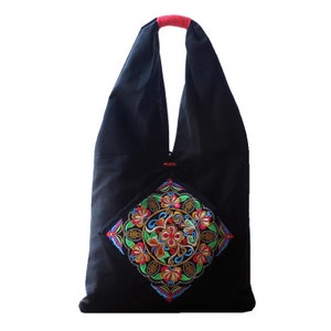 May include: A black tote bag with a vibrant, embroidered floral design in the center. The bag features a red handle and a diamond-shaped embroidered patch with colorful flowers and leaves. The bag is made of a soft material.