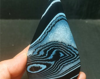 May include: A teardrop-shaped cabochon of black agate with white and blue banding. The agate has a polished surface and is translucent.