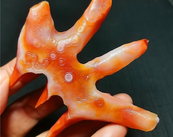 Pode incluir: Uma escultura de ágata laranja e branca vibrante em forma de árvore estilizada com detalhes intrincados. A escultura tem uma superfície lisa e polida e apresenta um padrão único de manchas brancas.