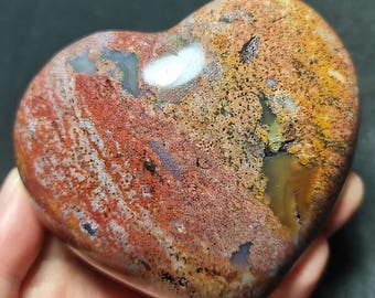 May include: A heart-shaped polished agate stone with a variety of colors, including red, orange, brown, white, and gray. The stone has a unique pattern of swirls and bands.