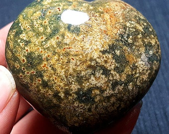 May include: A heart-shaped green, brown, and white moss agate stone. The stone has a smooth, polished surface.