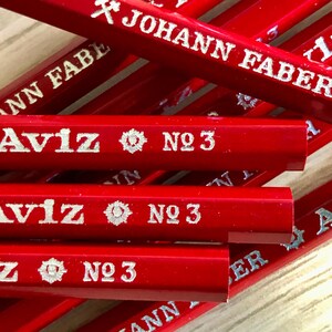 Może przedstawiać: Zbliżenie na stos czerwonych oł&oacute;wk&oacute;w z srebrnymi napisami. Oł&oacute;wki są oznaczone "Johann Faber" i "Aviz No. 3".