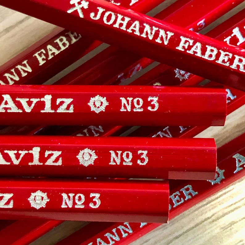 Może przedstawiać: Zbliżenie na stos czerwonych oł&oacute;wk&oacute;w z srebrnymi napisami. Oł&oacute;wki są oznaczone "Johann Faber" i "Aviz No. 3".