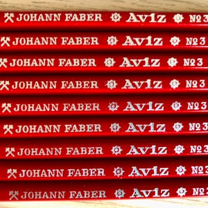 Może przedstawiać: Zbliżenie na osiem czerwonych oł&oacute;wk&oacute;w z srebrnym napisem. Oł&oacute;wki są oznaczone "JOHANN FABER Aviz N23".