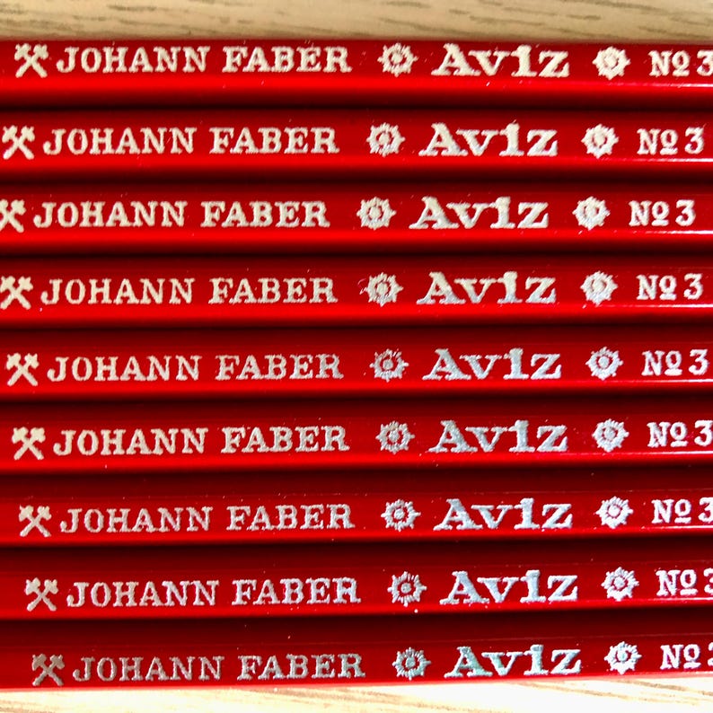 Może przedstawiać: Zbliżenie na osiem czerwonych oł&oacute;wk&oacute;w z srebrnym napisem. Oł&oacute;wki są oznaczone "JOHANN FABER Aviz N23".