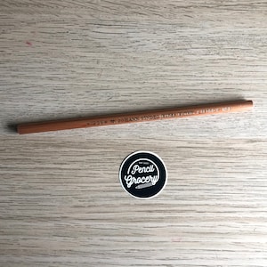 K&ouml;nnte beinhalten: Ein brauner Holzstift mit dem Aufdruck "#1205 = M. JOHANN SINDELGRABEN 131/D  +  G.D.R.O.C.  N92". Der Stift liegt auf einer hellbraunen Holzoberfl&auml;che. Ein schwarz-wei&szlig;er Aufkleber mit dem Text "Pencil Grocery" befindet sich in der unteren rechten Ecke des Bildes.