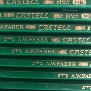 May include: Close-up of several green pencils with gold lettering. The pencils have the words "CASTELL" and "A.W. FABER" printed on them. The pencils are labeled "GERMANY" and "HB".