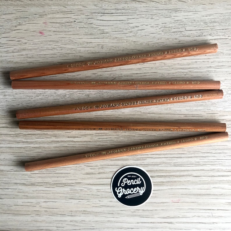 K&ouml;nnte beinhalten: F&uuml;nf braune Holzbleistifte mit goldener Beschriftung. Die Bleistifte sind mit "JOHANN SINDELGICH (CLOSE EXTRA) CEDRO N&deg;2" beschriftet.