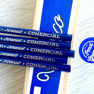 Puede incluir: Primer plano de cinco l&aacute;pices azules con letras doradas que dicen "*"Viarco"* COMERCIAL". Los l&aacute;pices est&aacute;n apilados uno encima del otro. Los l&aacute;pices est&aacute;n delante de una caja azul y blanca con la palabra "Pencil Gras" en un c&iacute;rculo.