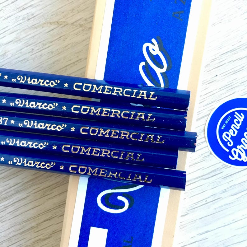 Puede incluir: Primer plano de cinco l&aacute;pices azules con letras doradas que dicen "*"Viarco"* COMERCIAL". Los l&aacute;pices est&aacute;n apilados uno encima del otro. Los l&aacute;pices est&aacute;n delante de una caja azul y blanca con la palabra "Pencil Gras" en un c&iacute;rculo.