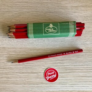 Może przedstawiać: Pudełko czerwonych oł&oacute;wk&oacute;w z logo Faber-Castell i pojedynczy czerwony oł&oacute;wek z napisem "JOHANN FABER AVIZ No. 3".