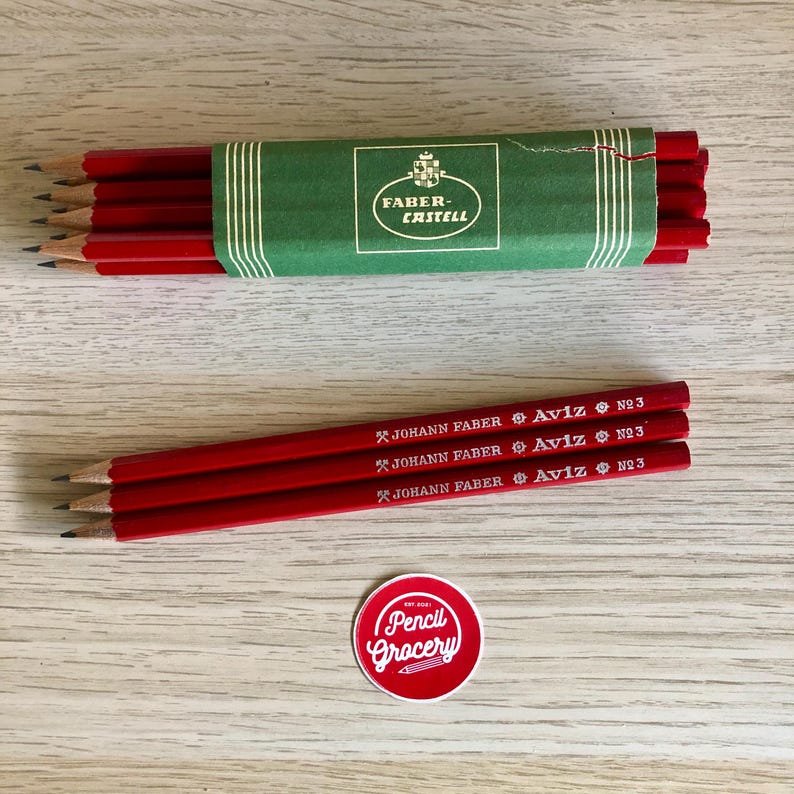 Może przedstawiać: Opakowanie czerwonych oł&oacute;wk&oacute;w z nadrukowaną nazwą marki "Faber-Castell". Widoczne są trzy pojedyncze oł&oacute;wki z nadrukowanym tekstem "JOHANN FABER Aviz N№3". Widoczna jest r&oacute;wnież naklejka z tekstem "Pencil Grocery".
