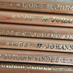 K&ouml;nnte beinhalten: Nahaufnahme von mehreren Bleistiften aus Holz mit goldener Beschriftung. Die Bleistifte sind mit "=1205= JOHANN SINDEL GLASE" beschriftet.