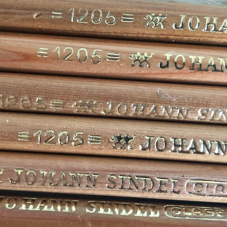 K&ouml;nnte beinhalten: Nahaufnahme von mehreren Bleistiften aus Holz mit goldener Beschriftung. Die Bleistifte sind mit "=1205= JOHANN SINDEL GLASE" beschriftet.