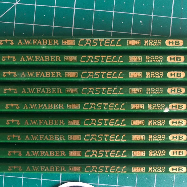 May include: A close-up shot of several green pencils with gold lettering. The pencils are labeled "A.W. Faber Castell 9000 HB Germany". The pencils are arranged in parallel rows on a green surface.