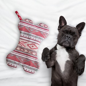May include: A black and white French bulldog dog is sleeping on a white bedspread. A red and white bone-shaped stocking is lying on the bedspread.
