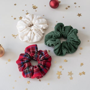 May include: Three fabric scrunchies in different patterns and colors. One is white, one is green, and one is red with a plaid pattern.