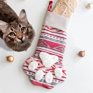 May include: A red and white striped Christmas stocking with a paw print design. The stocking has a white fluffy lining and is decorated with a green and white pattern.
