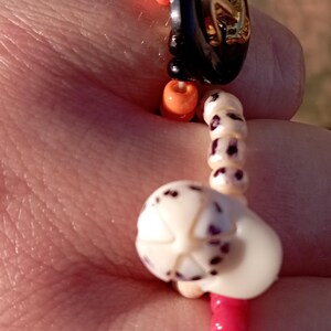May include: A beaded bracelet with a nautical theme. The bracelet features blue, orange, black, and white beads. A black button with a gold anchor design is a focal point. The bracelet is approximately 7 inches in length.