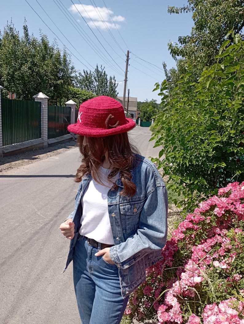 May include: A red crochet hat with a wide brim, adorned with white and brown decorative elements. The hat is a vibrant shade of red, perfect for sun protection. The hat is a stylish accessory.
