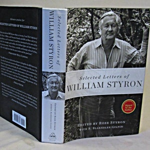 May include: A black and white photo of William Styron on the cover of his book "Selected Letters of William Styron". The book cover features a white background with black text and a red stamp that says "Signed by the Author".