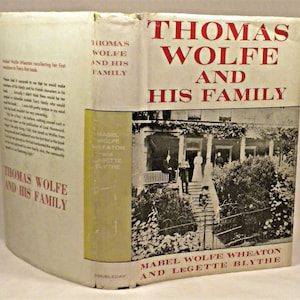 May include: A vintage book cover with a black and white photo of a house with a porch and steps. The title of the book is "Thomas Wolfe and His Family" and the authors are Mabel Wolfe Wheaton and Legette Blythe.