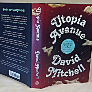 May include: A book cover for the novel "Utopia Avenue" by David Mitchell, a New York Times bestselling author. The cover features a stylized title in white and black stripes against a dark red background with white clouds and stars.