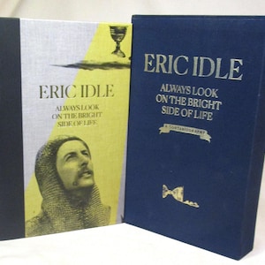 May include: Two hardcover books by Eric Idle. One book has a navy blue cover with gold lettering and the title "Always Look on the Bright Side of Life." The other book has a yellow and silver cover with the same title and a portrait.