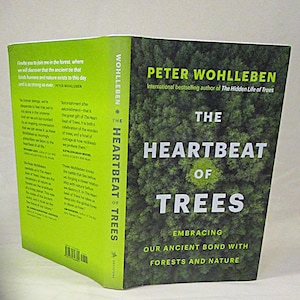 Puede incluir: Un libro de tapa dura titulado The Heartbeat of Trees de Peter Wohlleben. La portada muestra un denso dosel forestal verde con texto en blanco. El lomo y la contraportada de color verde lima incluyen testimonios impresos y un código de barras.