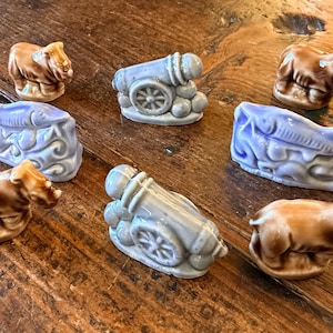 May include: A collection of small ceramic figurines in various shapes, including cannons, rhinos, and fish. The figurines are primarily brown and blue, with a glossy finish. They are arranged on a wooden surface.