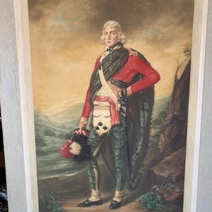 May include: A framed print of a man in a red jacket and plaid trousers, holding a hat. The artwork features a landscape background with mountains and a cloudy sky. The man wears a sash and carries a sword. The print is signed in the bottom right corner.
