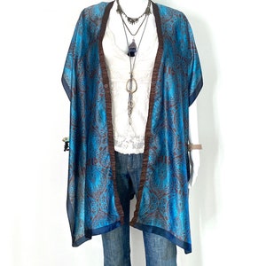 May include: A blue and brown patterned silk kimono with a dark blue trim. The kimono is open in the front and has a white lace top underneath. The model is wearing blue jeans.