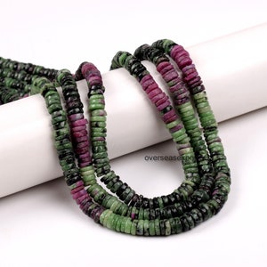 May include: Strands of gemstone beads in shades of green, black, and magenta. The beads are flat, disc-shaped, and strung together. The beads are likely used for jewelry making.