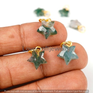 May include: Close-up of several star-shaped pendants. The pendants are made of green and white stone with gold-coloured loops. The pendants are held in a hand. The text "Love Craftjewell" is visible.