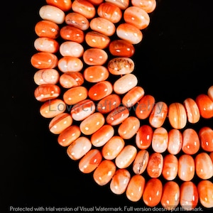 May include: A close-up shot of a necklace made of orange and white oval beads. The beads are smooth and glossy, with a mix of colours. The background is black, which makes the beads stand out.