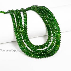 May include: Multiple strands of bright green gemstone beads are shown against a white backdrop. The beads are small, round, and polished. The image is well-lit, emphasising the colour and texture of the gemstones. These beads are likely used for jewellery making, such as necklaces or bracelets.