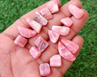 May include: A collection of small, polished rhodochrosite stones in various shades of pink and white. Each stone features unique banded patterns and smooth, irregular shapes. The stones are displayed together, showcasing their natural color variations.