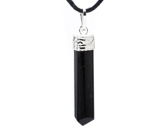 Puede incluir: Un collar con colgante de turmalina negra. La gema cilíndrica pulida está rematada con metal plateado y cuelga de un cordón negro. El colgante tiene un extremo facetado y puntiagudo. El fondo es blanco.