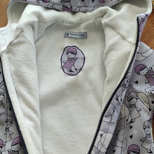 Könnte beinhalten: Eine graue Kapuzenjacke mit einem weißen Fleecefutter. Die Jacke hat einen Reißverschluss und ein kleines gesticktes Schild mit der Aufschrift "Ressie Design". Der Stoff hat ein sich wiederholendes Muster aus Mädchen, die Eisbären mit Herzen halten.