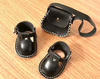 May include: Two black leather shoes with white stitching and a black leather satchel with white stitching.