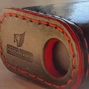 May include: Close-up of a black leather case with red stitching. The case has a red circle cutout and the text "Passion Leather" with a winged logo.