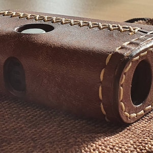 Könnte beinhalten: Eine braune Ledertasche mit weißen Nähten und einem Ausschnitt für ein Gerät. Die Tasche liegt auf einer braunen Jutestoffe.