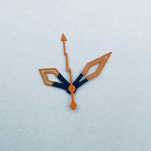 Puede incluir: Manecillas de reloj naranja y negro con una manecilla de hora puntiaguda y una manecilla de minutos en forma de diamante.