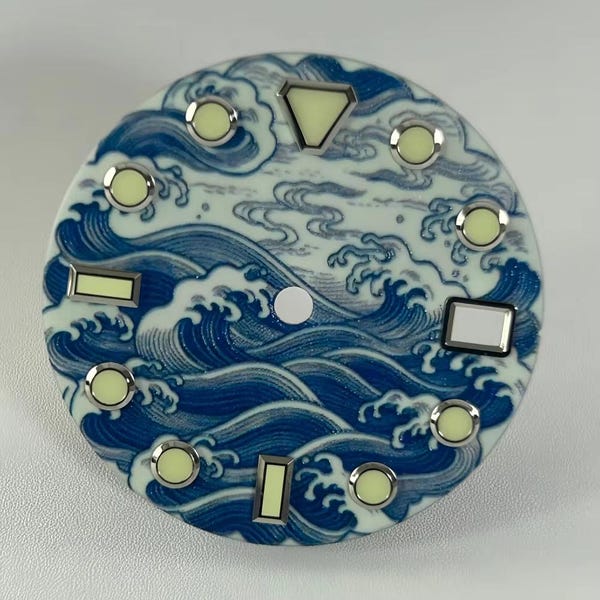 May include: A circular watch dial featuring a blue and white wave pattern. The dial includes silver-rimmed hour markers with pale yellow luminous centers, including a triangular marker at the top, rectangular markers, and circular markers.