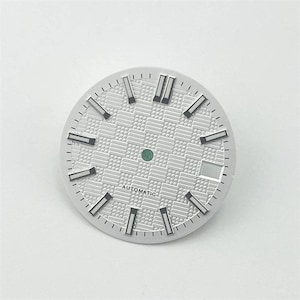 Può includere: Un quadrante per orologio circolare argentato con motivo a scacchiera testurizzato, indici a bastone argentati applicati con dettagli neri, un perno centrale, una finestrella per la data a ore tre e la parola AUTOMATIC stampata in nero.