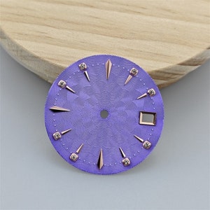 K&ouml;nnte beinhalten: Ein violettes Zifferblatt mit ros&eacute;goldenen Akzenten und Diamant-Stundenmarkierungen.